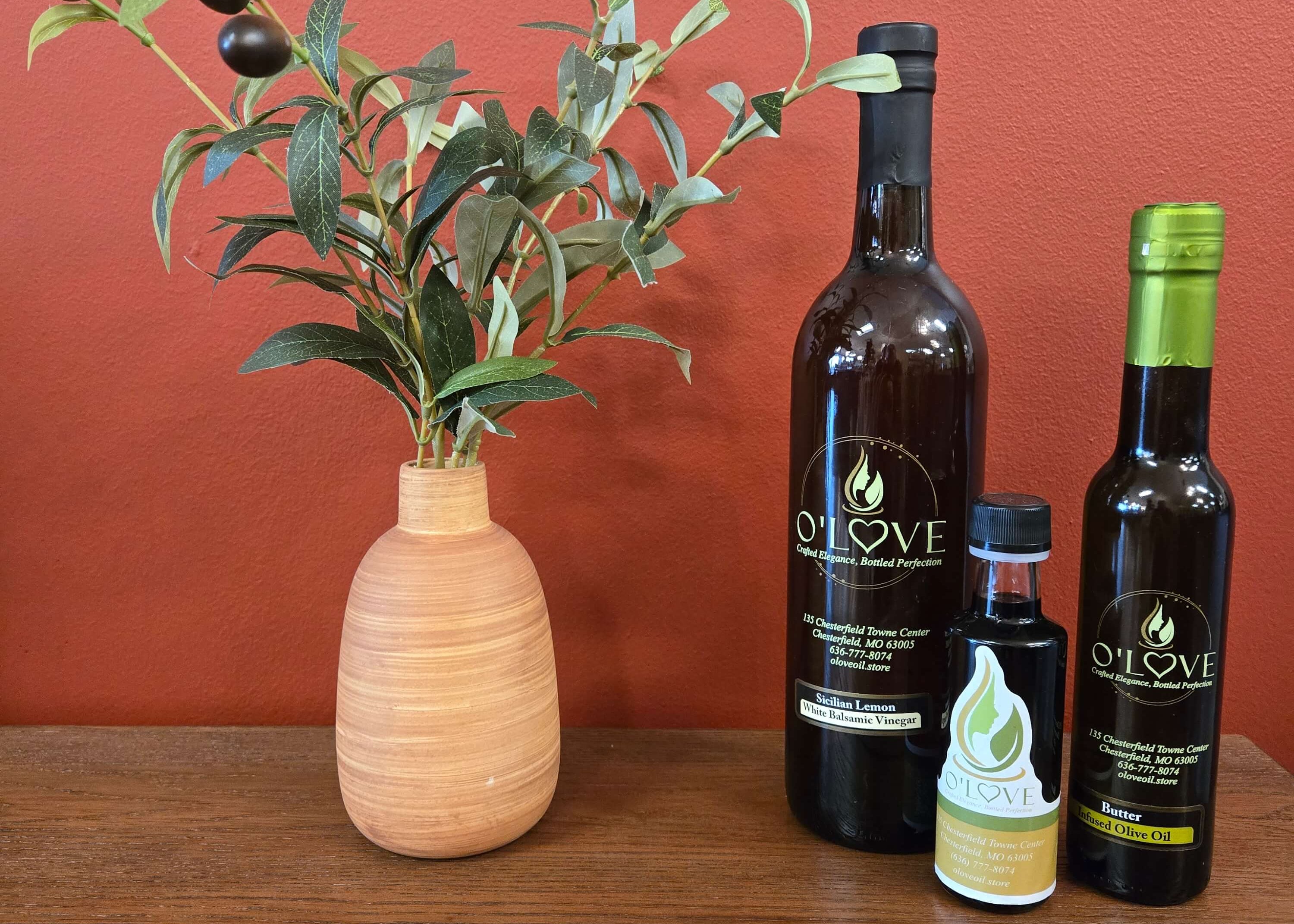 Three bottles of of olive oil and vinegar next to fake olive plant